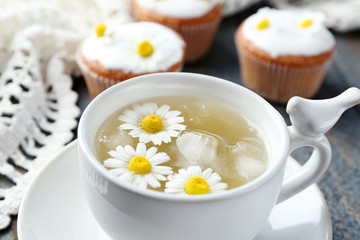 Cup of chamomile tea with chamomile flowers and tasty muffins  on color wooden background