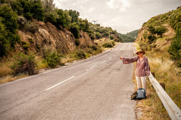 Fototapeta premium Woman hitchhiker with straw hat by the road during vacation in the Mediterranean