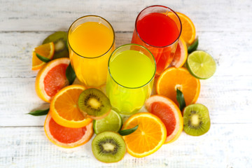 Glasses of different juice with fruits and mint on wooden background