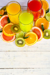 Glasses of different juice with fruits and mint on wooden background
