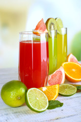 Glasses of different juice with fruits and mint on bright background