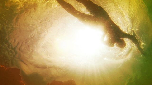 An underwater shot of a swimming man against bright sunshine