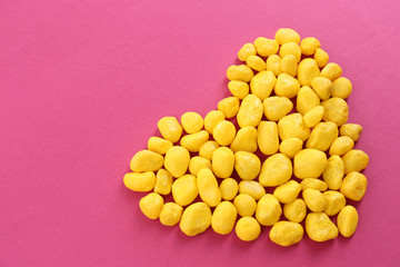 Sweet colorful candies in heart shape on pink background