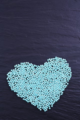 Colorful beads in heart shape on grey background