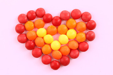 Sweet colorful candies in heart shape on pink background