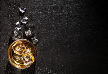 Glass of whiskey with ice on black stone table
