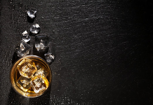 Glass Of Whiskey With Ice On Black Stone Table