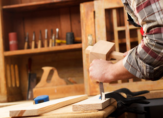 Closeup of a carpenter working with a hammer, chisel and wood carving tools.