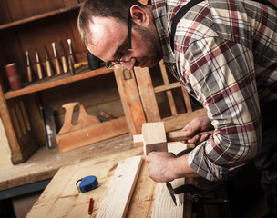 Closeup of a carpenter working with a hammer, chisel and wood carving tools.