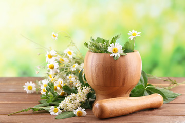 Naklejka na ściany i meble Herbs and flowers with mortar, on wooden table, on bright background
