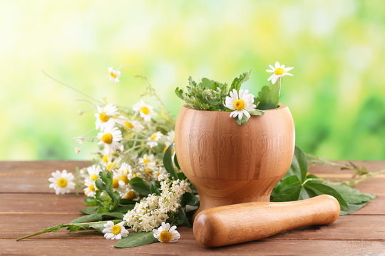 Herbs and flowers with mortar, on wooden table, on bright background