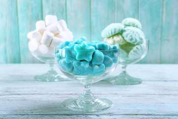 Fluffy candies in glassware on wooden background