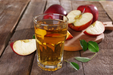 Glass of apple juice with red apples on wooden table, closeup