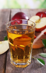 Glass of apple juice with red apples on wooden table, closeup