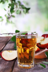 Glass of apple juice with red apples on wooden table on blurred background