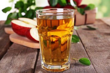 Glass of apple juice with red apples on wooden table, closeup