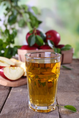 Glass of apple juice with red apples on wooden table on blurred background