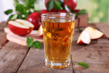 Glass of apple juice with red apples on wooden table, closeup