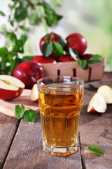 Glass of apple juice with red apples on wooden table on blurred background