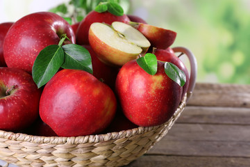 Naklejka na ściany i meble Red apple in wicker basket on wooden table, closeup