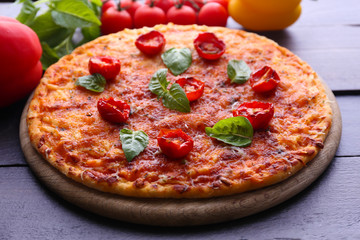 Pizza with basil and cherry tomatoes on wooden table, closeup