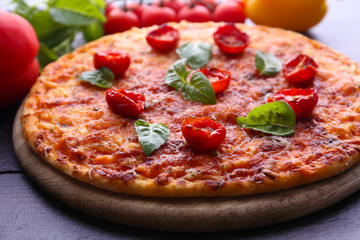 Pizza with basil and cherry tomatoes on wooden cutting board, closeup