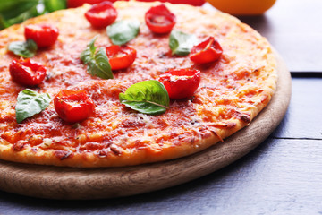 Pizza with basil and cherry tomatoes on wooden cutting board, closeup