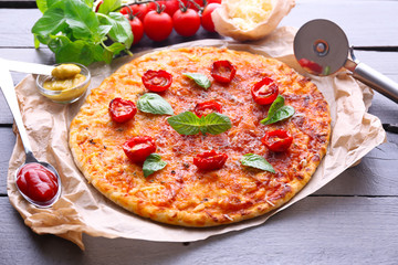 Pizza with basil and cherry tomatoes on parchment on wooden table, closeup