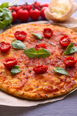 Pizza with basil and cherry tomatoes on parchment on wooden table, closeup