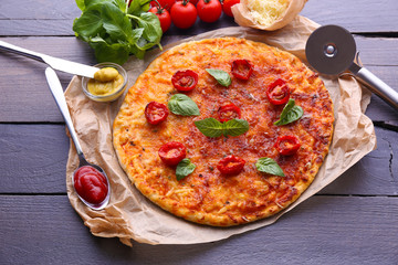 Pizza with basil and cherry tomatoes on parchment on wooden table background