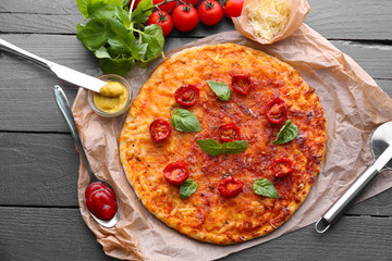 Pizza with basil and cherry tomatoes on parchment on wooden table, closeup