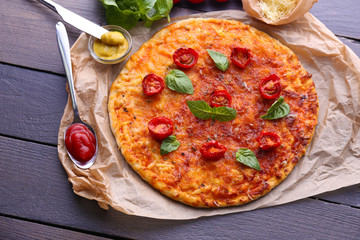 Pizza with basil and cherry tomatoes on parchment on wooden table, closeup