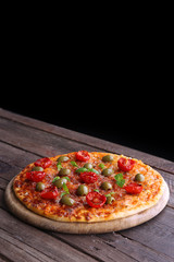Tasty pizza with cherry tomatoes, green olives and herbs on wooden table on black background