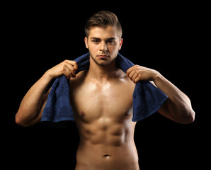 Fototapeta premium Muscle young man holding towel on dark background