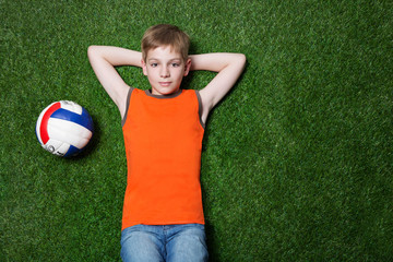 Boy lying with ball on green grass