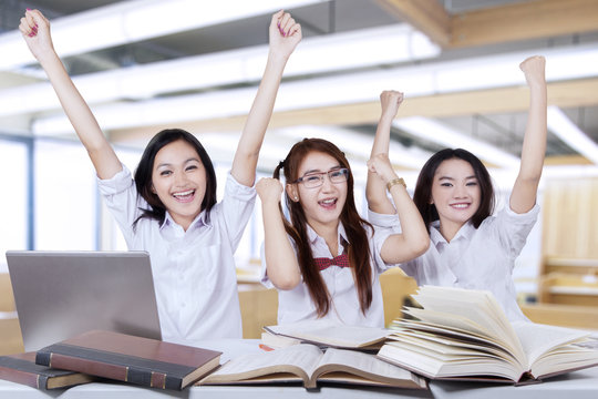 Three happy students raise hands in class
