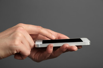 Hands holding mobile smart phone on gray background