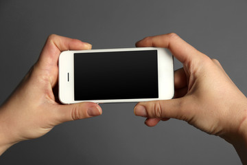 Hands holding mobile smart phone on gray background