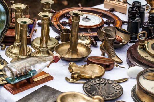 display of old brass candleholders,ashtrays,miniature boats on glass bottle and other brass objects for collection sold at flea market for antique collection