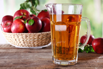 Full jug of apple juice and fruits on bright background