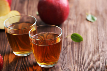 Glasses of apple juice and fruits on table close up