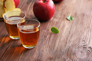 Glasses of apple juice and fruits on table close up