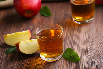 Glasses of apple juice and fruits on table close up