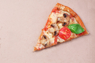 Slice of tasty pizza with vegetables and basil in cardboard close up