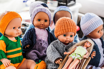 display of old plastic dolls and baby dolls wearing home-made knitwear sold at flea market or...