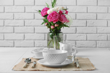 Beautiful table setting with flowers in vase on brick wall background