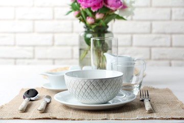 Beautiful table setting with flowers in vase on brick wall background