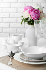 Beautiful table setting with flowers in vase on brick wall background
