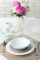 Beautiful table setting with flowers in vase on brick wall background