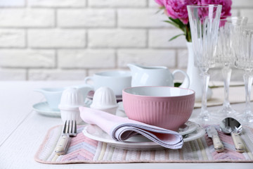 Beautiful table setting with flowers in vase on brick wall background